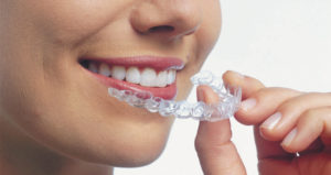 A woman holding a clear aligner near her mouth, smiling softly