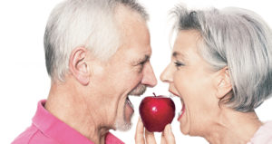 Close-up of a married couple with their faces close together, about to take a bite of a red appl