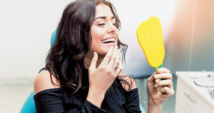 Female patient examining her teeth using a dental mirror during a check-up