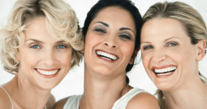 Three caucasian women heads together smiling with beautiful white healthy smiles